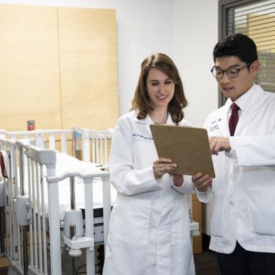 Physicians in white lab coats reviewing records on a clipboard.