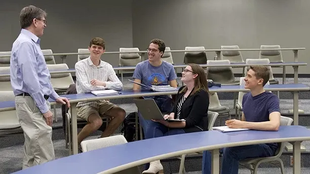 Students talking with a professor in a classroom.