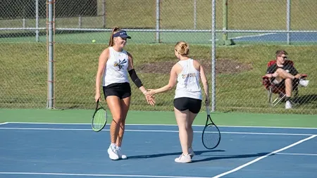 Two girls high five on tennis court