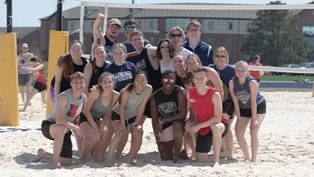 Group of students smiling on sand volleyball court