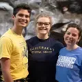 Threestudentssmilinginfrontofclimbingwall