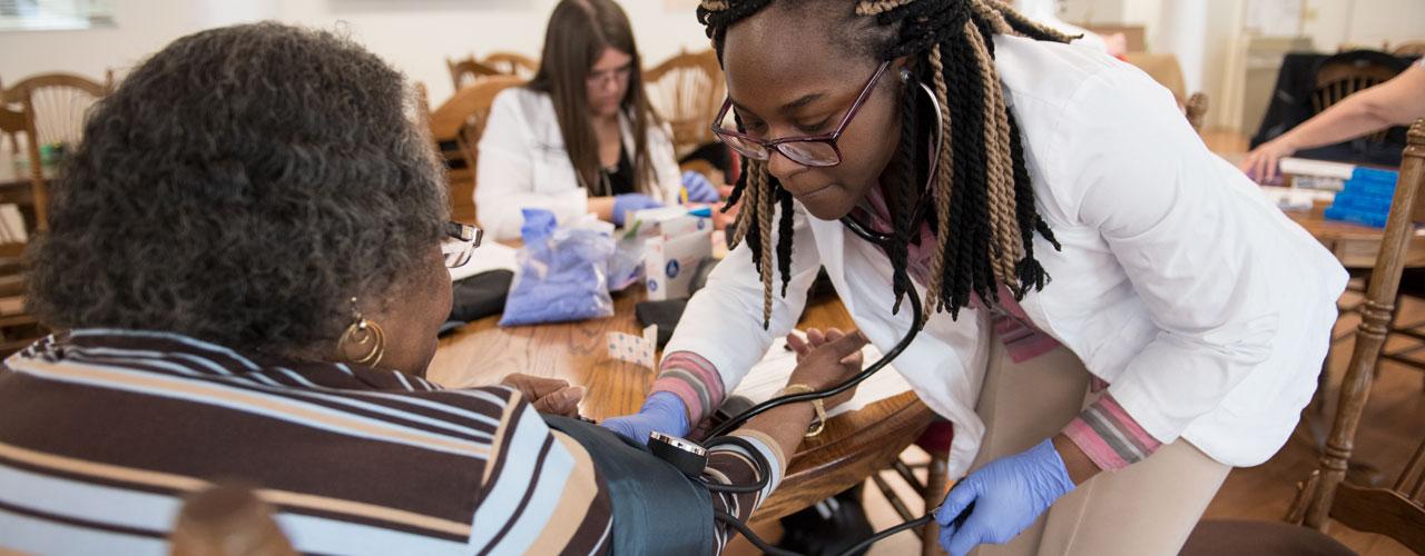 A female Doctor of Pharmacy student is checking a patient's blood pressure