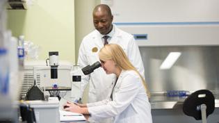 Pharmacy Professor instructs student how to use microscope